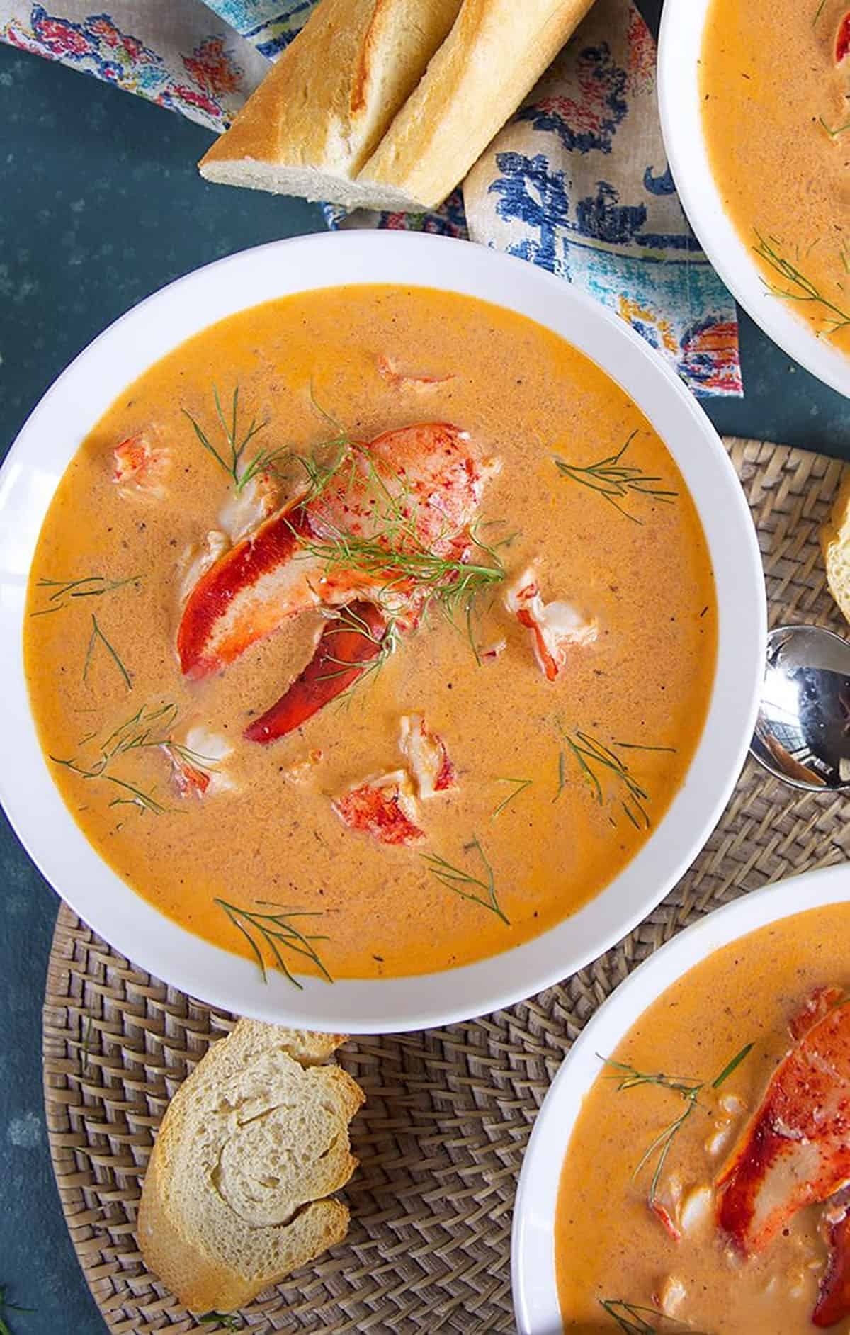 Overhead shot of Lobster Bisque in a white bowl with bread on the side and a lobster claw in the center of the soup.