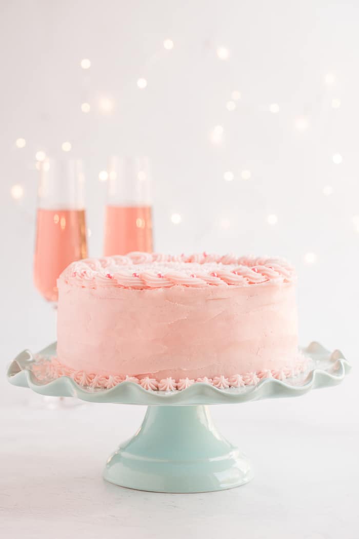 Pink Champagne Cake on a mint green cake stand on a white background with twinkle lights.