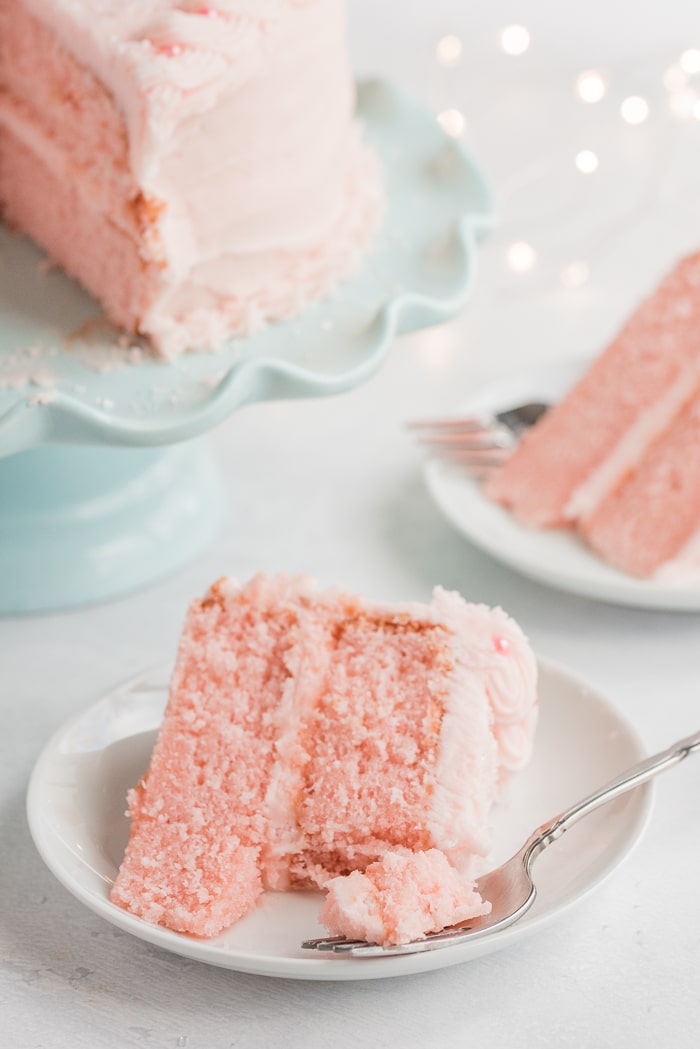 Slice of pink champagne cake on a white plate with a bite on a fork.