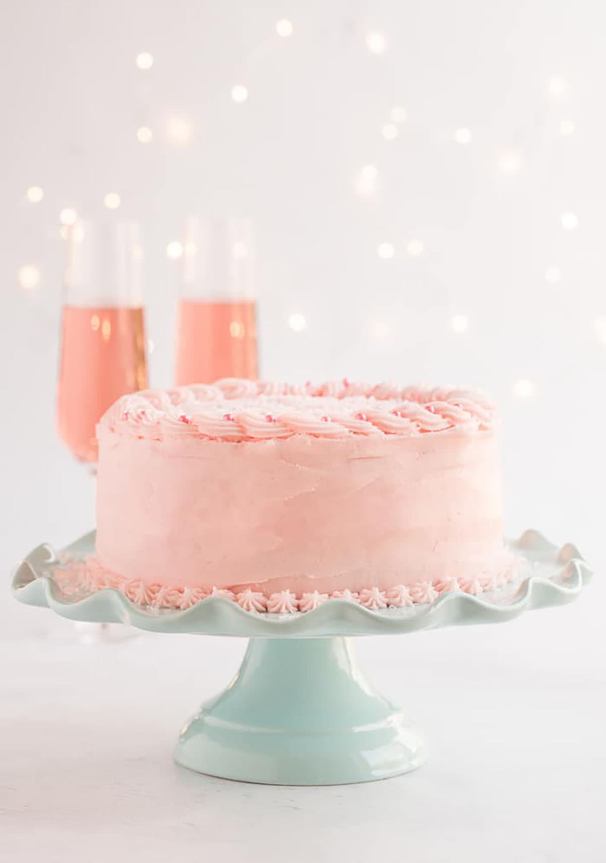 Pink Champagne Cake on a mint green cake stand on a white background with twinkle lights.