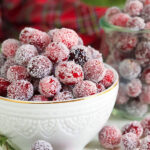 Sugared Cranberries in a white bowl with a red plaid napkin in the background.