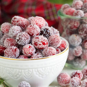 Sugared Cranberries in a white bowl with a red plaid napkin in the background.