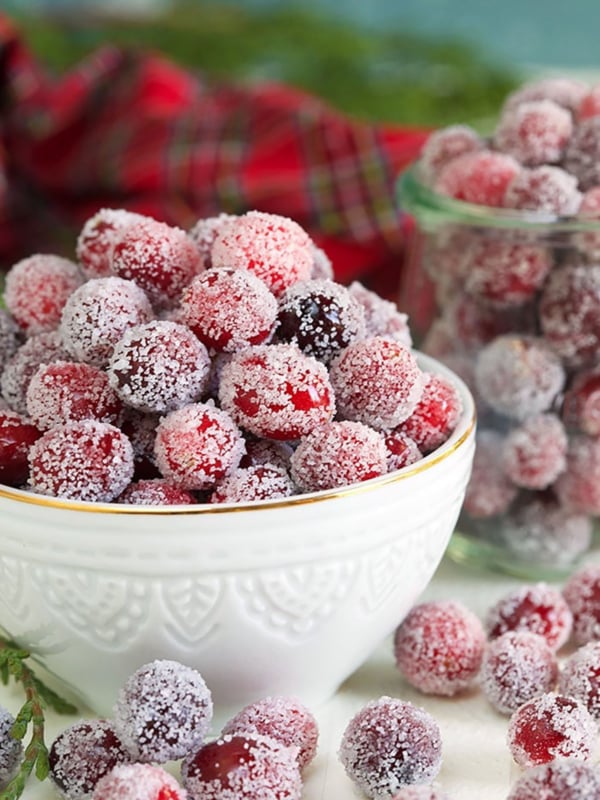 Sugared Cranberries in a white bowl with a red plaid napkin in the background.