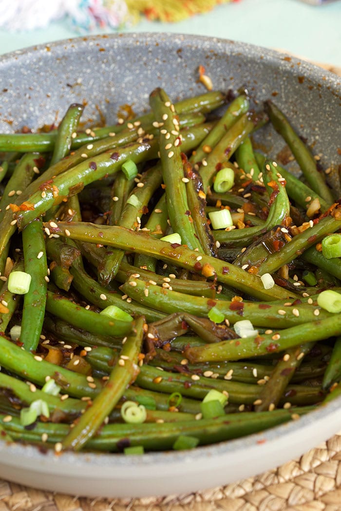 Chopped green onions and sesame seeds garnish a bowl of green beans.