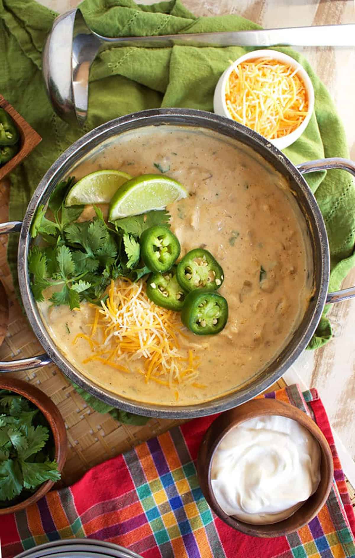 pot of white chicken chili with sliced jalapenos, cilantro, cheese and two lime wedges.