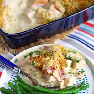 A plate with a serving of chicken cordon bleu casserole with green beans and a blue fork.