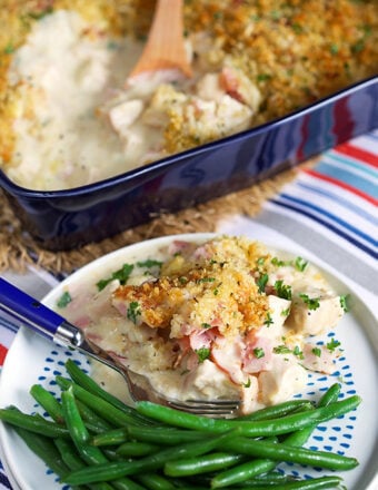 A plate with a serving of chicken cordon bleu casserole with green beans and a blue fork.