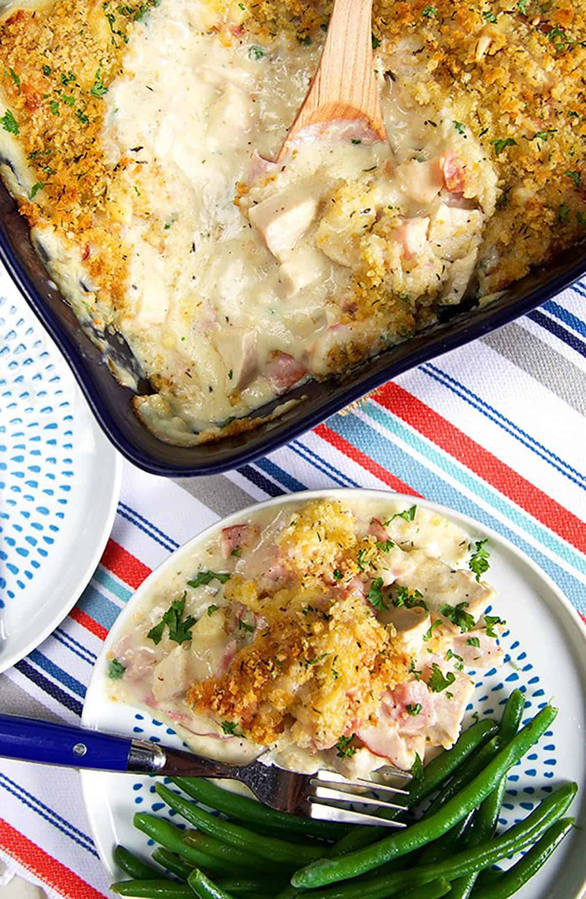 Overhead shot of Chicken Cordon Bleu Casserole in a navy baking dish and a serving on a plate with green beans.