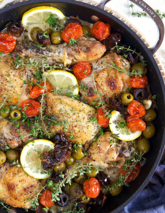 Chicken thighs, lemons and olives are prepared in a large black skillet.