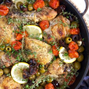 Chicken thighs, lemons and olives are prepared in a large black skillet.