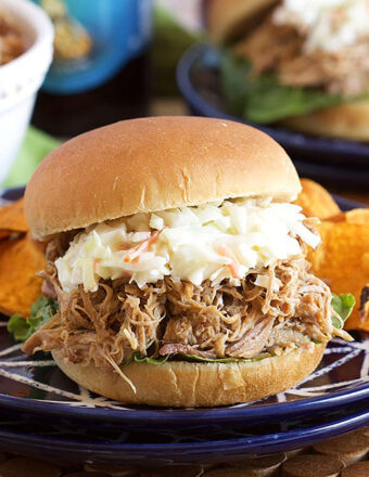 Pulled Pork Sandwich with coleslaw on top and placed on a blue and white plate with sweet potato chips.