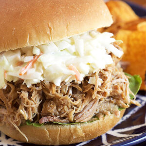 Closeup of pulled pork sandwich with coleslaw on top on a blue plate.