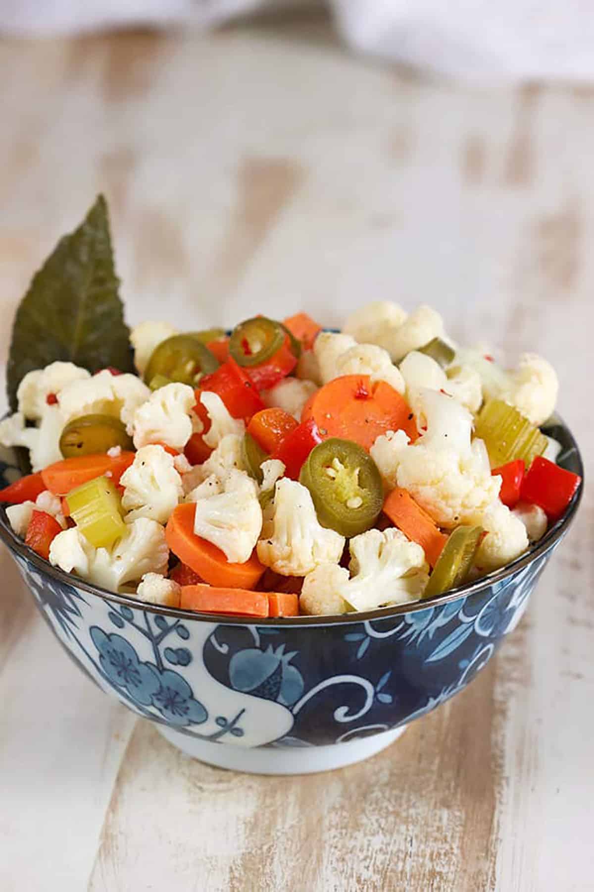 Giardiniera in a blue and white bowl with a bay leaf on the side.