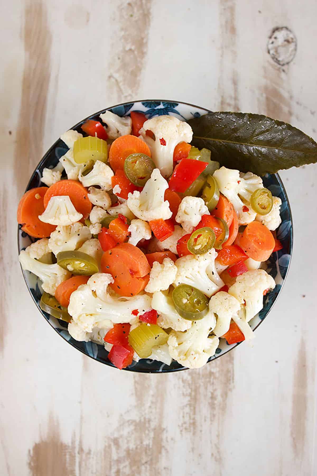 Giardiniera with a bay leaf in a blue and white bowl on a distressed wood backdrop.