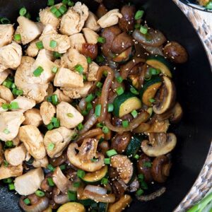 Chicken and veggies are in a large skillet, garnished with chopped green onions.