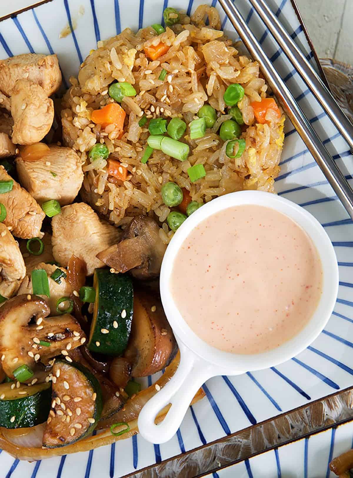 Fried rice is served with yum yum sauce and hibachi chicken.