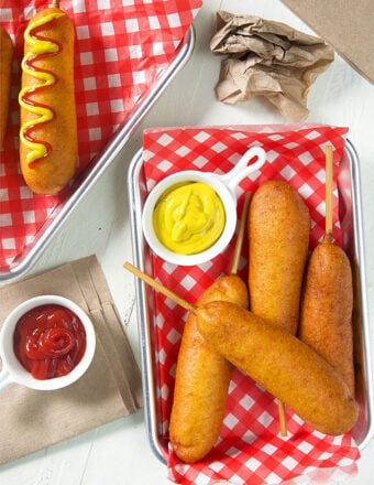 overhead shot of corn dogs on red and white paper with a dish of mustard.