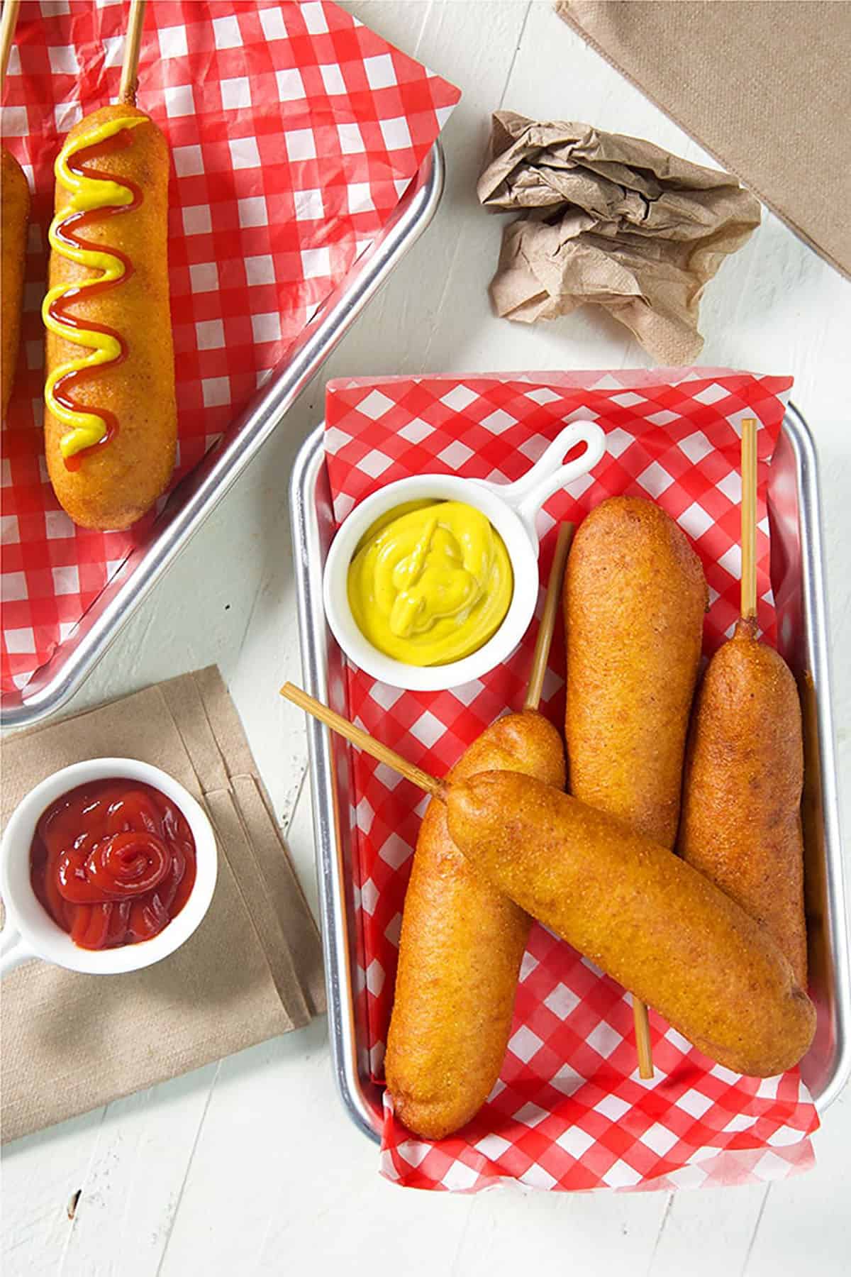 overhead shot of corn dogs on red and white paper with a dish of mustard.