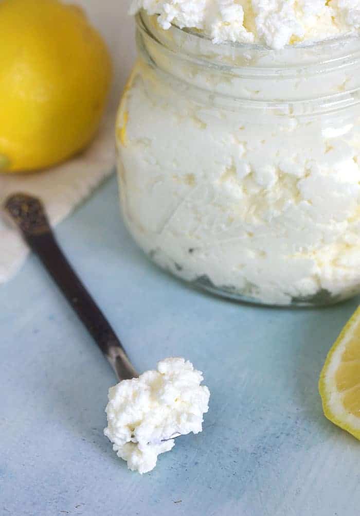A small spoon has scooped a portion of ricotta cheese from a glass jar.