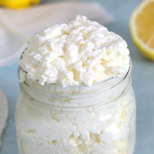 A glass jar of ricotta cheese is on a counter with sliced lemons.