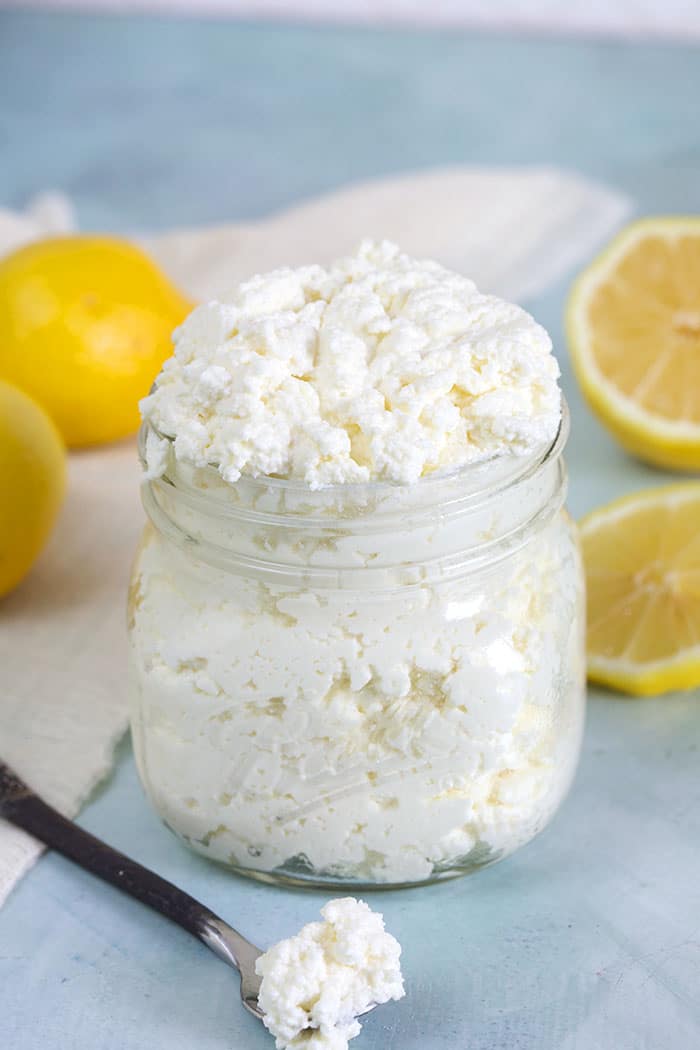 A little spoon with ricotta cheese sits next to an open jar on a blue countertop.