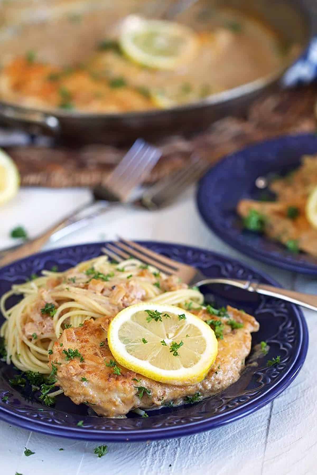 Lemon chicken scallopini on a blue plate with a skillet in the background.