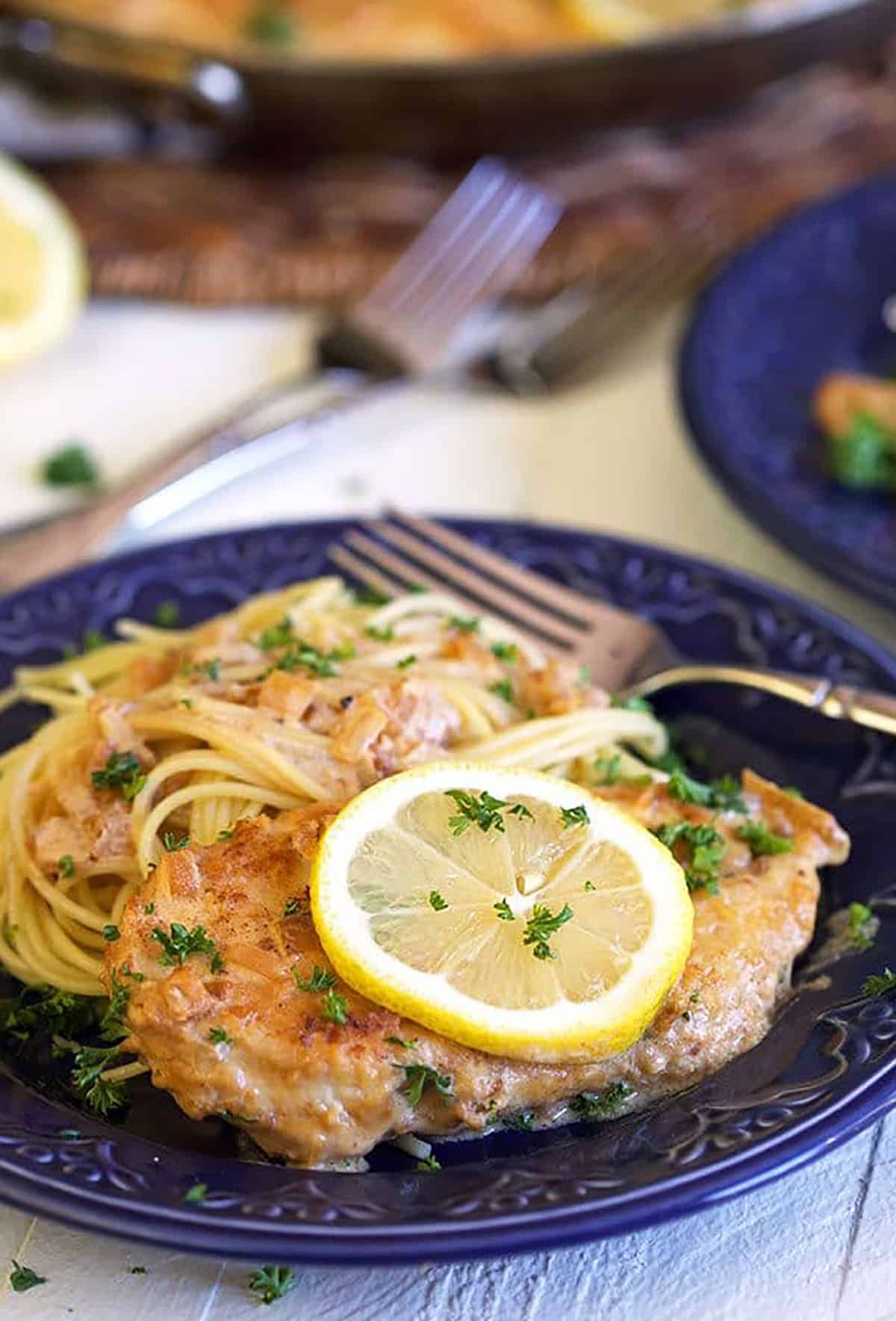 Lemon Chicken Scallopini on a blue plate with spaghetti and a lemon slice on top