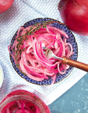 overhead shot of pickled red onions in a blue and white bowl on a white towel.