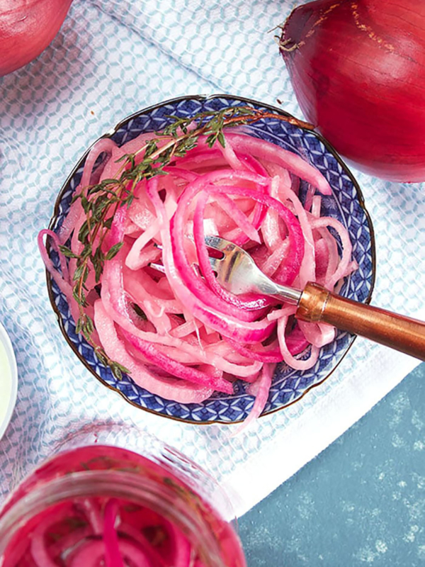 overhead shot of pickled red onions in a blue and white bowl on a white towel.