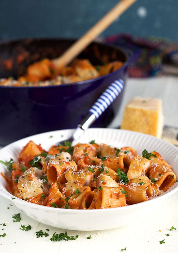 A striped fork is placed in a white bowl full of spicy rigatoni pasta.