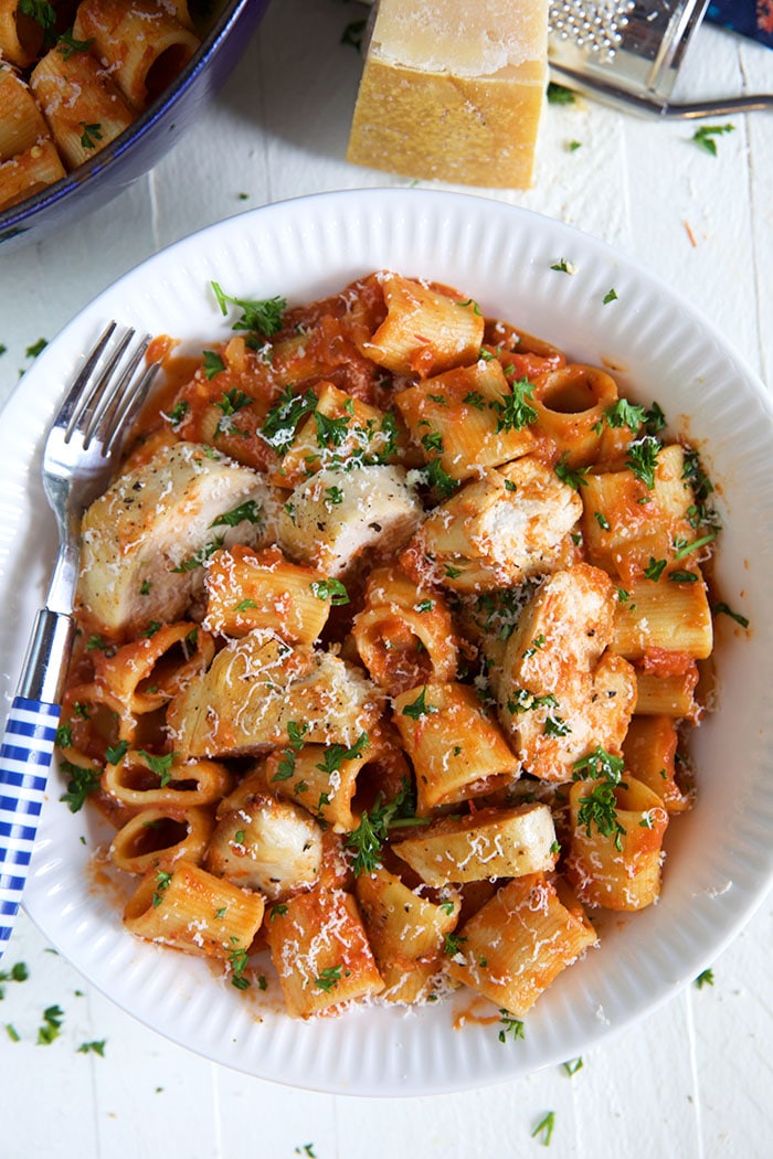A bowl of spicy rigatoni pasta is garnished with shaved parmesan and parsley.