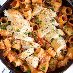 Sliced, cooked chicken breast sits on top of a skillet of spicy rigatoni.