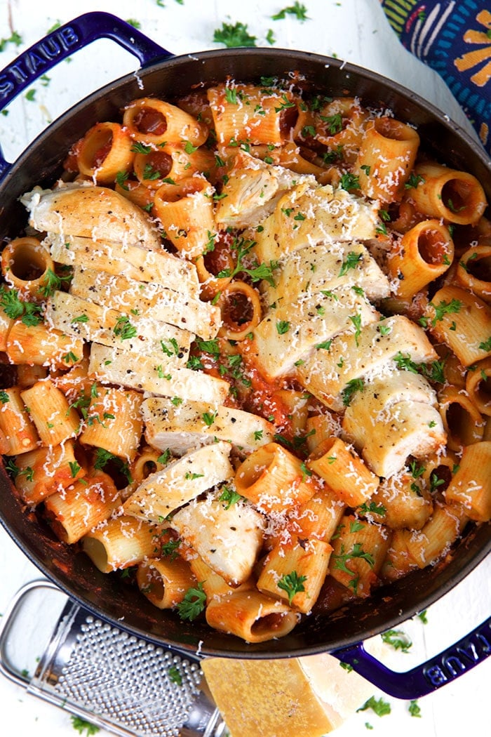 Sliced, cooked chicken breast sits on top of a skillet of spicy rigatoni.