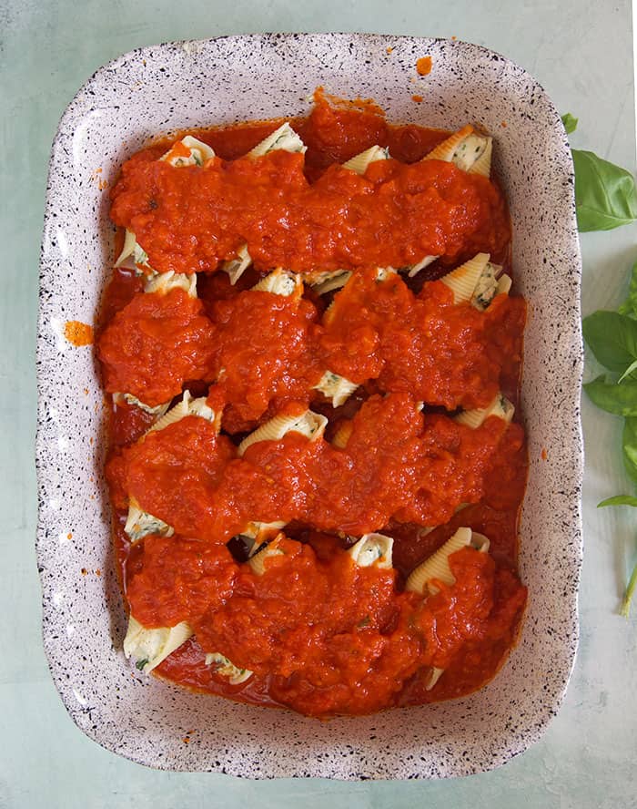 Stuffed shells are covered in red sauce in a large baking dish.