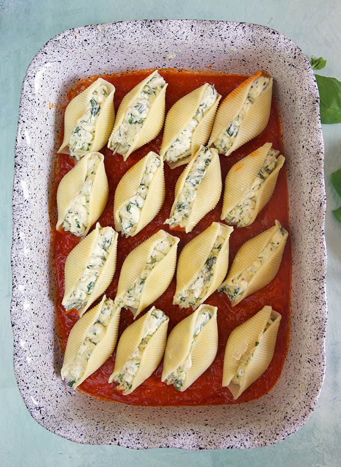Stuffed shells are placed in rows of four on top of a bed of red sauce in a baking dish.