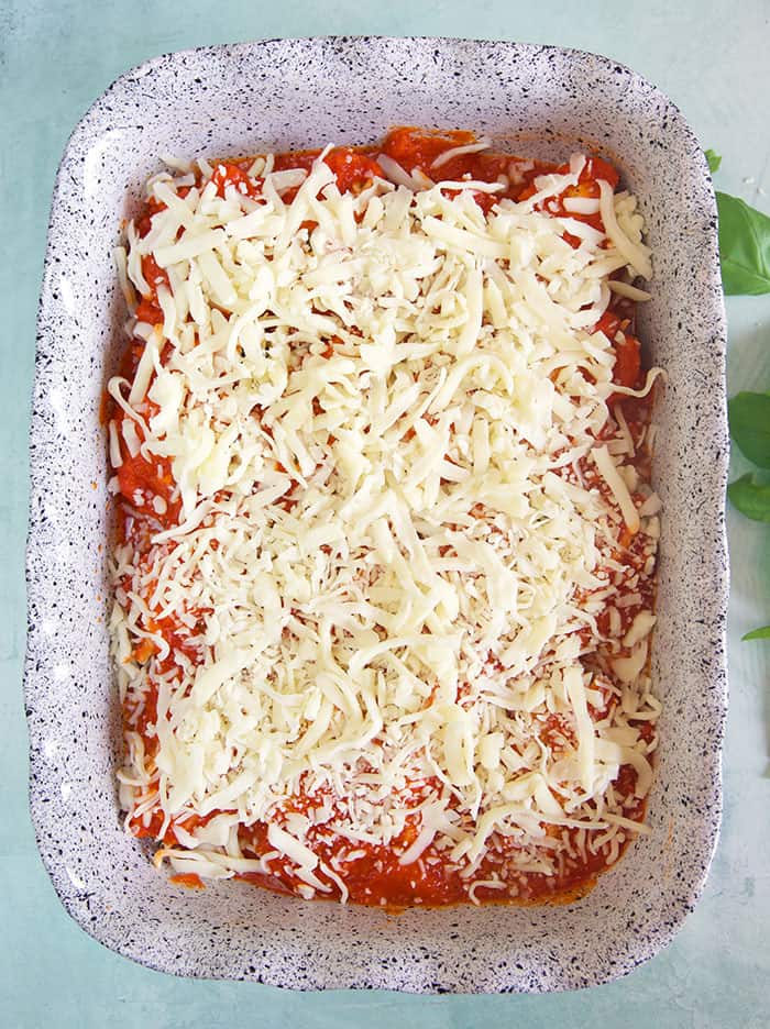 Shredded cheese covers the red sauce and shells in the baking dish.