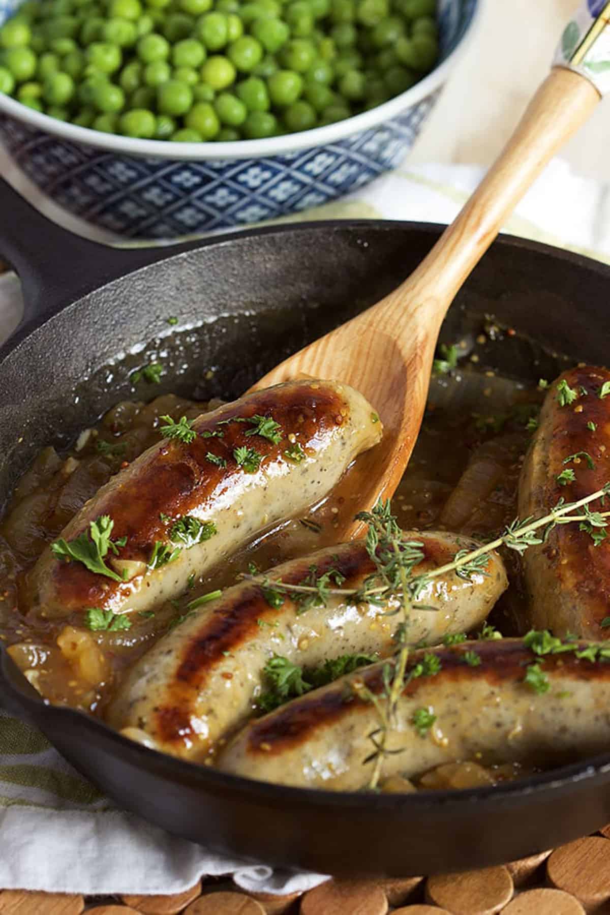4 sausages in a cast iron skillet with gravy and topped with sprigs of thyme.