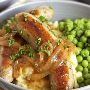 Two bangers on a pile of mashed potatoes with green peas. Onion gravy on top of the sausages.