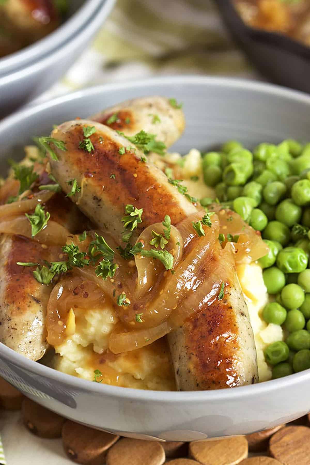 Two bangers on a pile of mashed potatoes with green peas. Onion gravy on top of the sausages.