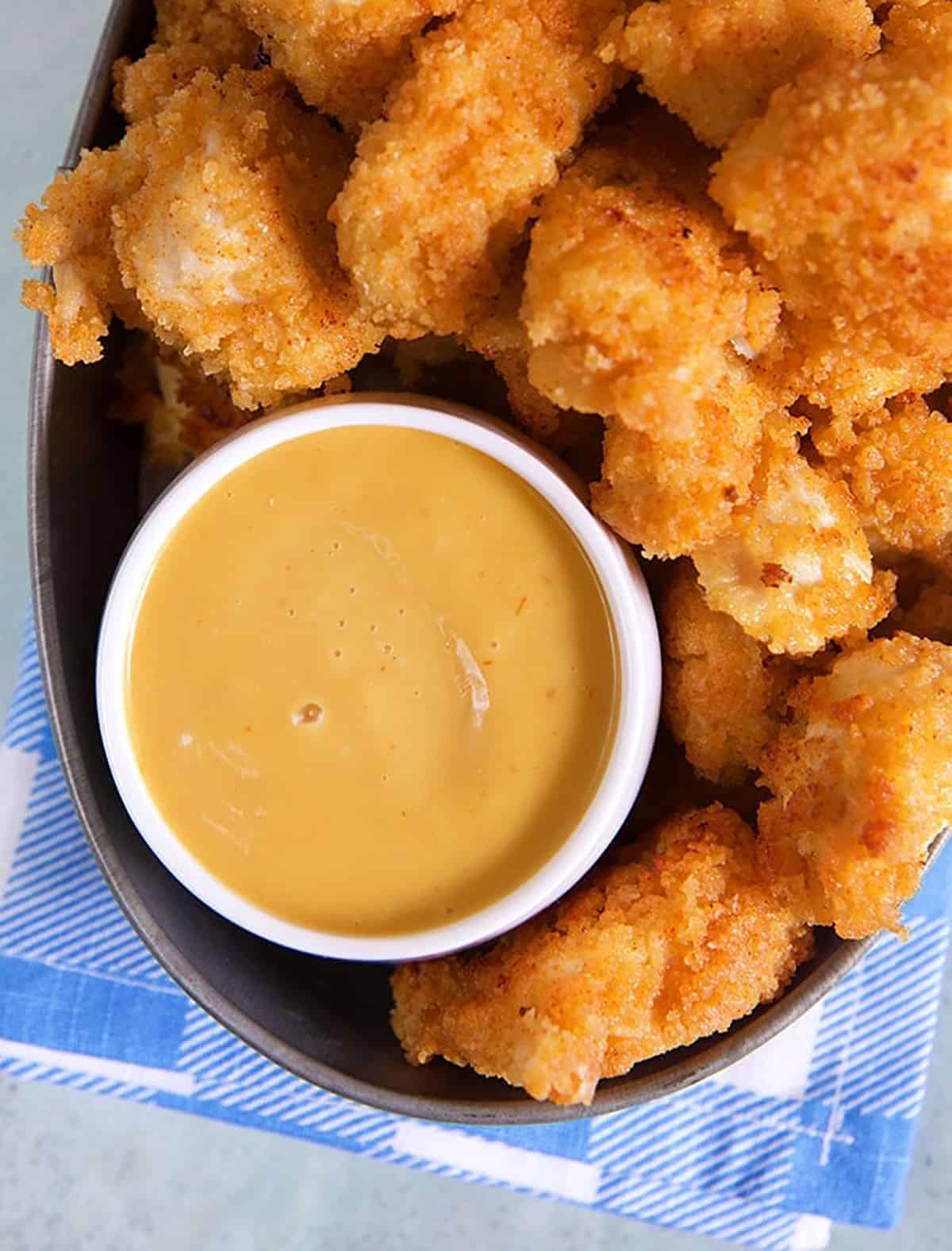 Chick Fil A sauce in a white dish with chicken nuggets around it on a blue napkin.