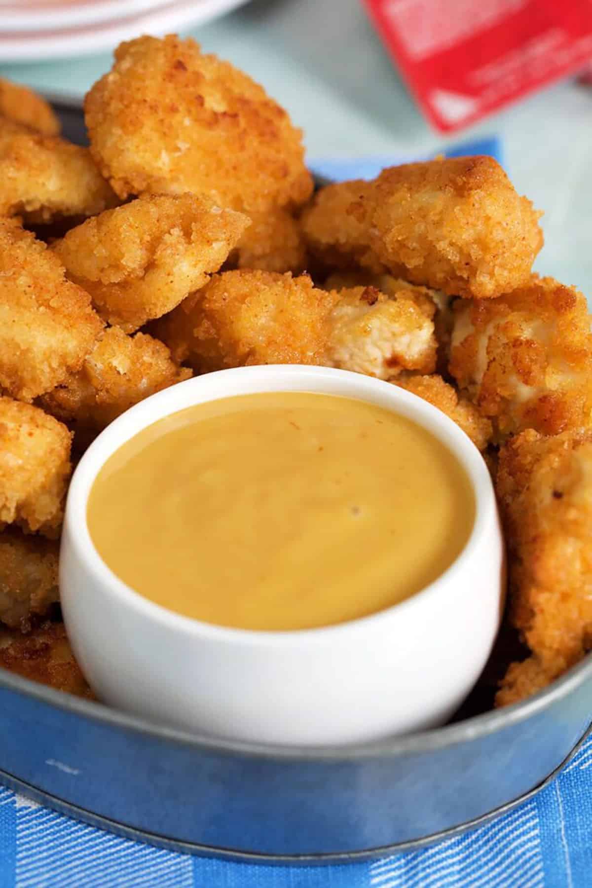 Chick Fil A Sauce in a white round dish inside a steel tray with chicken nuggets around the dish.