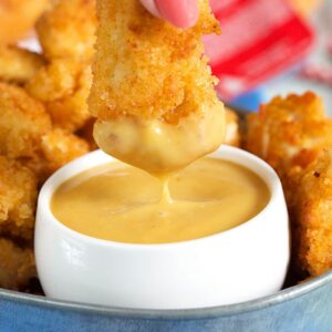 A chicken nugget is covered in yellow sauce.