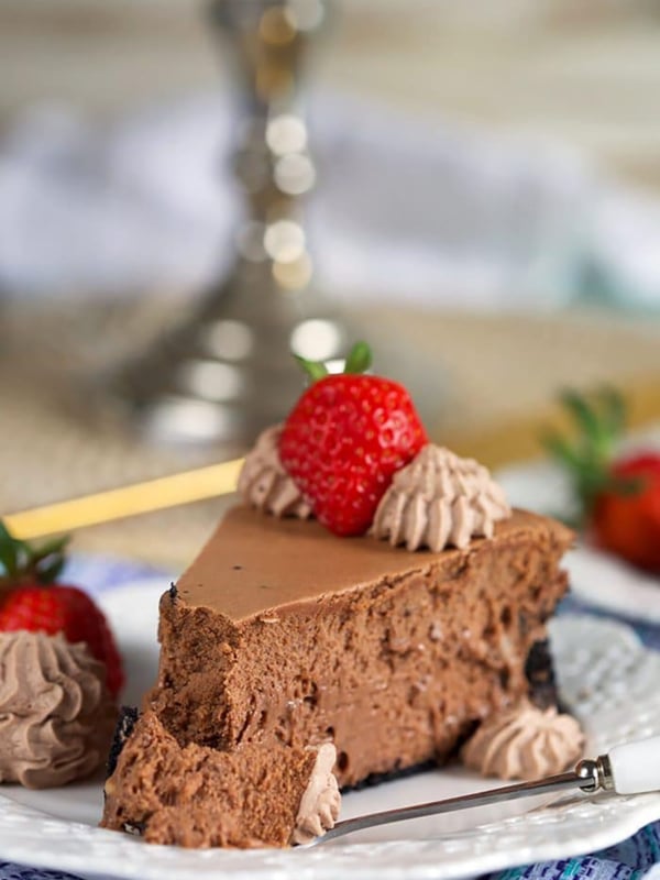 Slice of Chocolate Cheesecake with a strawberry on top and bite on a fork.