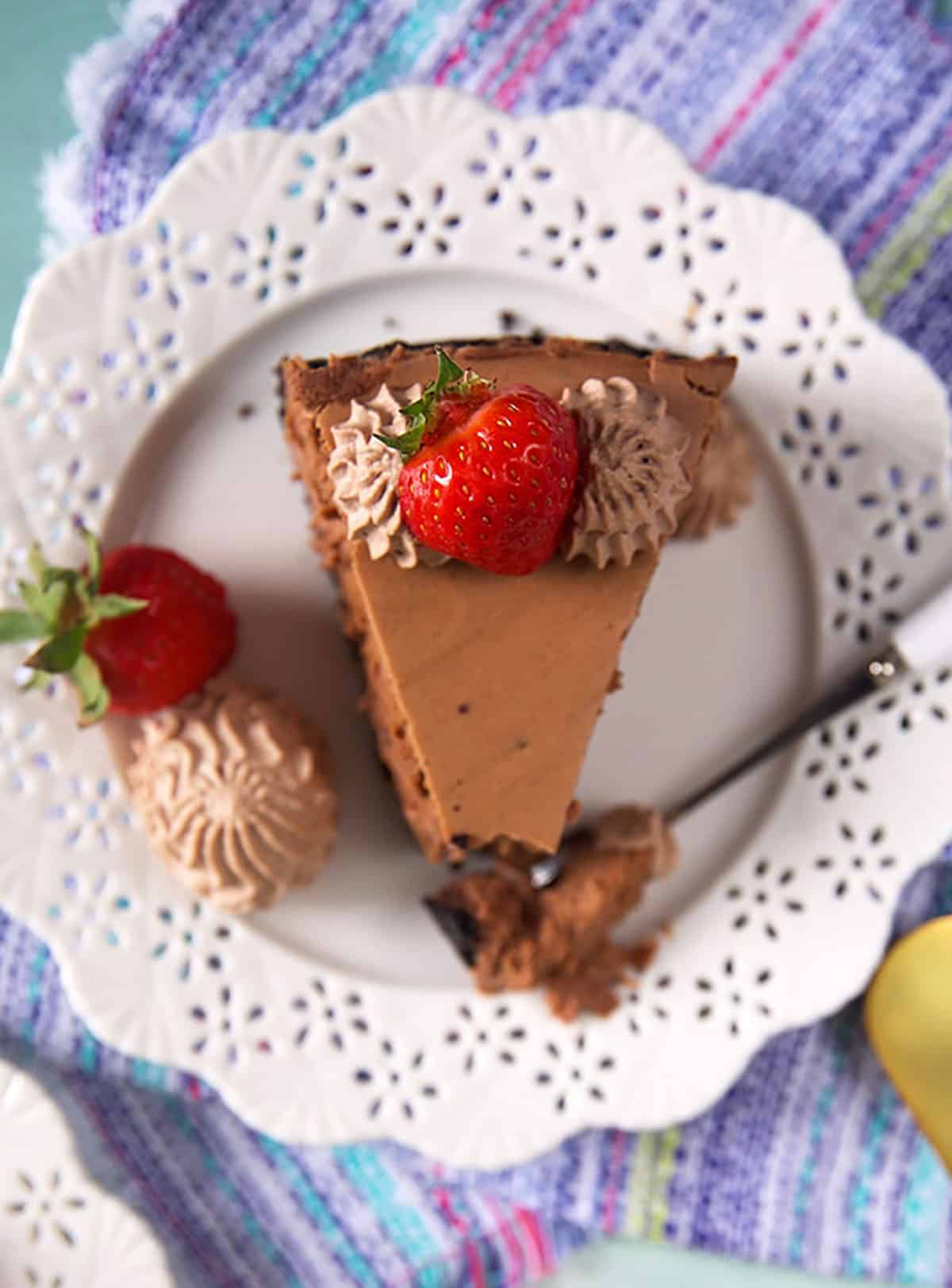 Overhead shot of a slice of chocolate cheesecake with a strawberry on top on a white plate.