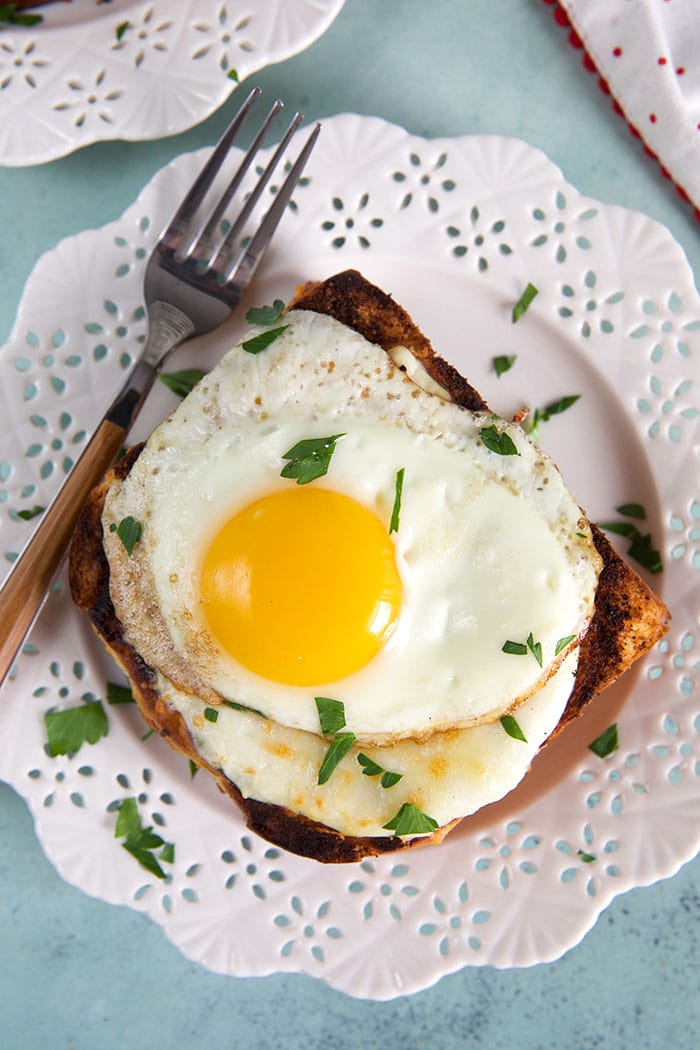 croque madame on a white plate with a fork on a blue background.