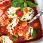 A large metal spoon is lifting a serving of gnocchi out of a pan.