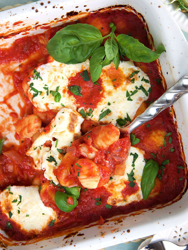 A large metal spoon is lifting a serving of gnocchi out of a pan.