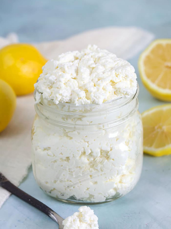 A little spoon with ricotta cheese sits next to an open jar on a blue countertop.