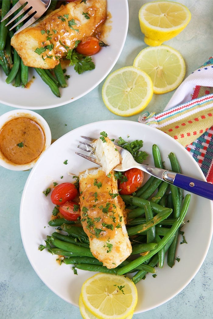 Two plates are on a table, both containing servings of halibut and green beans.
