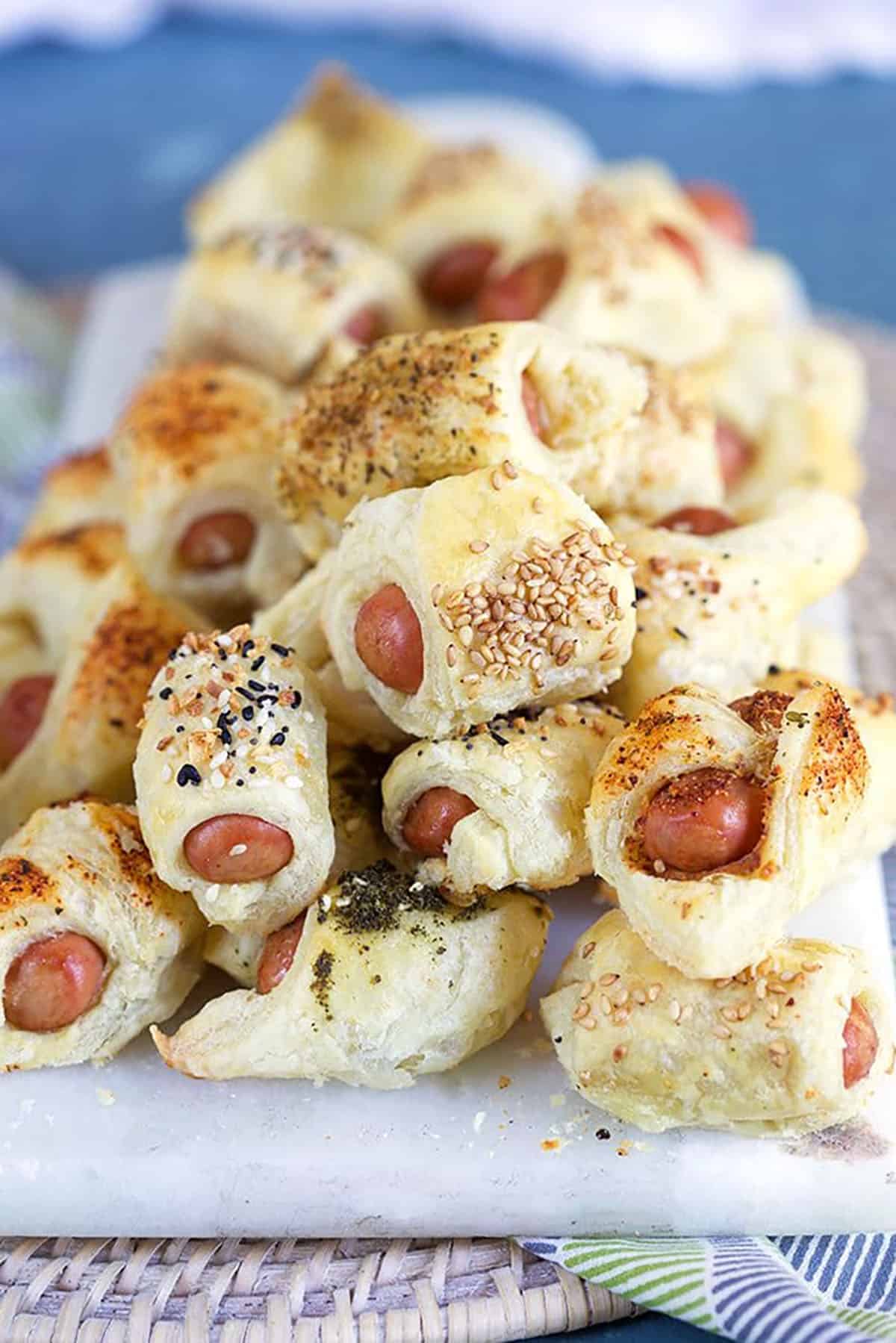 Pile of pigs in a blanket with seasonings on a marble tray.